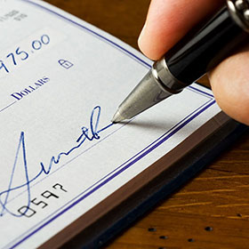 Close up of a person signing a check. Links to Gifts of Cash, Checks, and Credit Cards